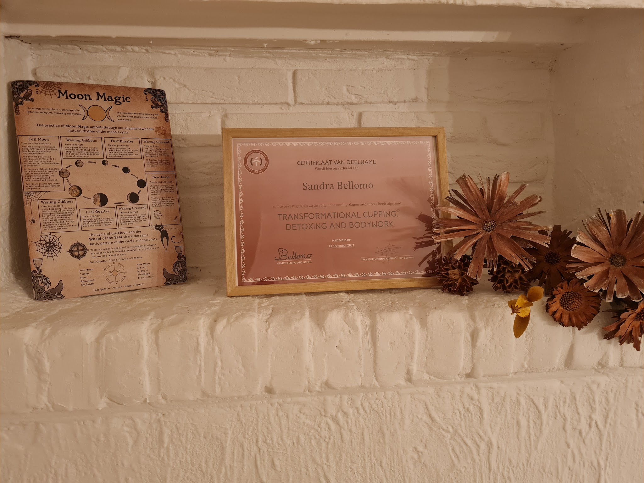 Nis in de witte stenen muur met een ingelijst certificaat, een Moon Magic-bord en gedroogde bloemen